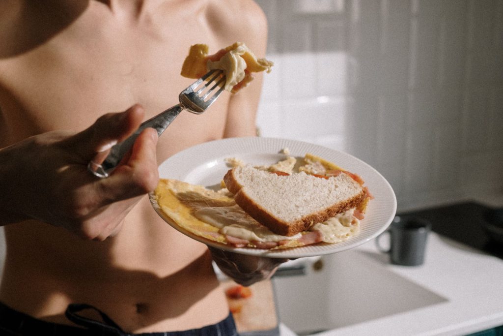 Mand spiser omelet med brød i køkkenet