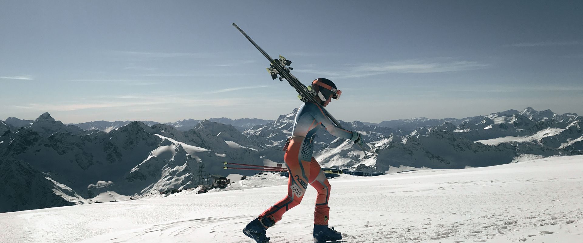 Mand i skistøvler bærer ski gennem sneen i bjergene
