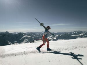 Mand i skistøvler bærer ski gennem sneen i bjergene